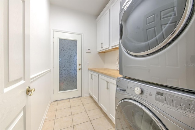 washroom featuring stacked washer / drying machine, cabinet space, baseboards, and light tile patterned flooring