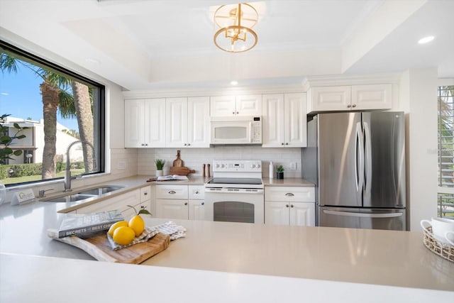 kitchen featuring a raised ceiling, light countertops, white cabinetry, a sink, and white appliances