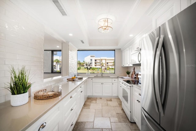 kitchen featuring a tray ceiling, light countertops, white cabinets, a sink, and white appliances