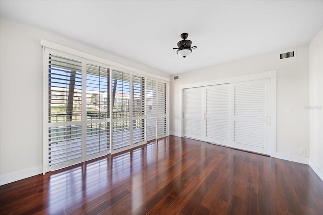 unfurnished bedroom with baseboards, visible vents, dark wood finished floors, access to outside, and a closet