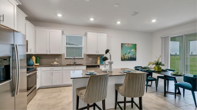 kitchen featuring a breakfast bar area, stainless steel appliances, a sink, white cabinets, and a center island