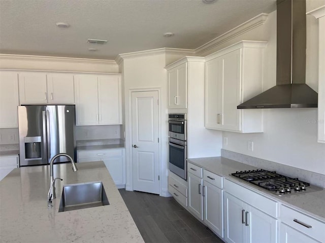 kitchen featuring visible vents, a sink, stainless steel appliances, white cabinets, and wall chimney range hood