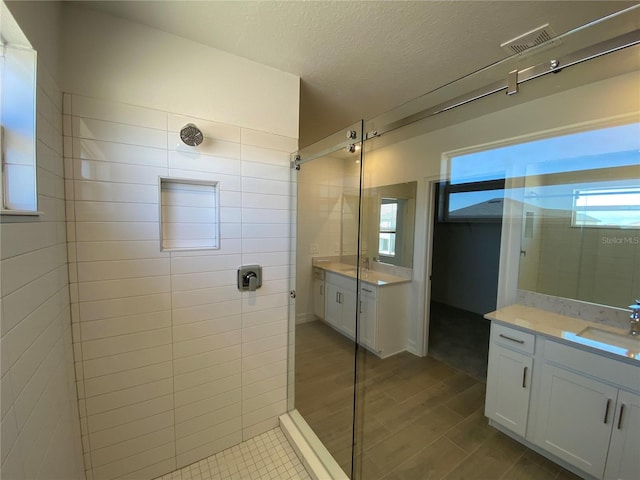 bathroom with vanity, visible vents, wood finish floors, a tile shower, and a textured ceiling