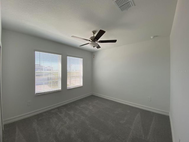 unfurnished room featuring visible vents, baseboards, ceiling fan, dark carpet, and a textured ceiling