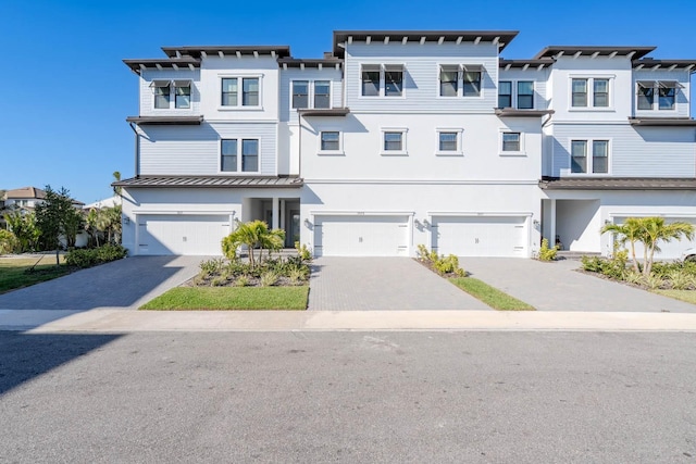 townhome / multi-family property with stucco siding, a standing seam roof, a garage, a residential view, and driveway