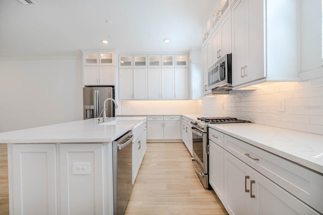 kitchen with stainless steel appliances, tasteful backsplash, an island with sink, and white cabinets