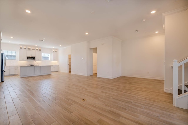 unfurnished living room with light wood-style floors, recessed lighting, baseboards, and stairs