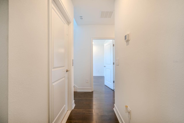 hall with dark wood-type flooring, visible vents, and baseboards