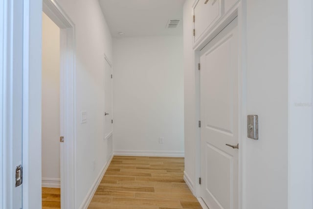 hallway with light wood finished floors, visible vents, and baseboards