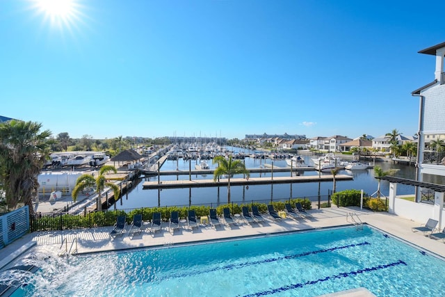 community pool with a patio area, a water view, and fence