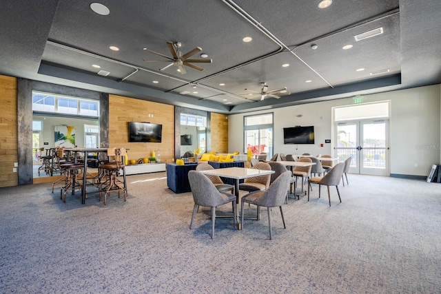 carpeted dining space with wood walls, visible vents, french doors, a wealth of natural light, and a tray ceiling