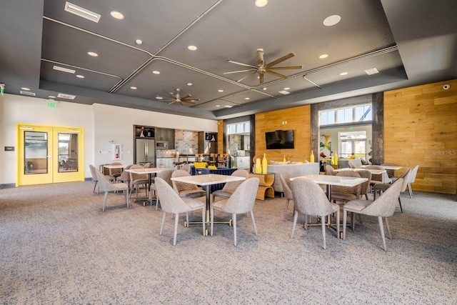 dining area featuring french doors, a raised ceiling, visible vents, ceiling fan, and wooden walls