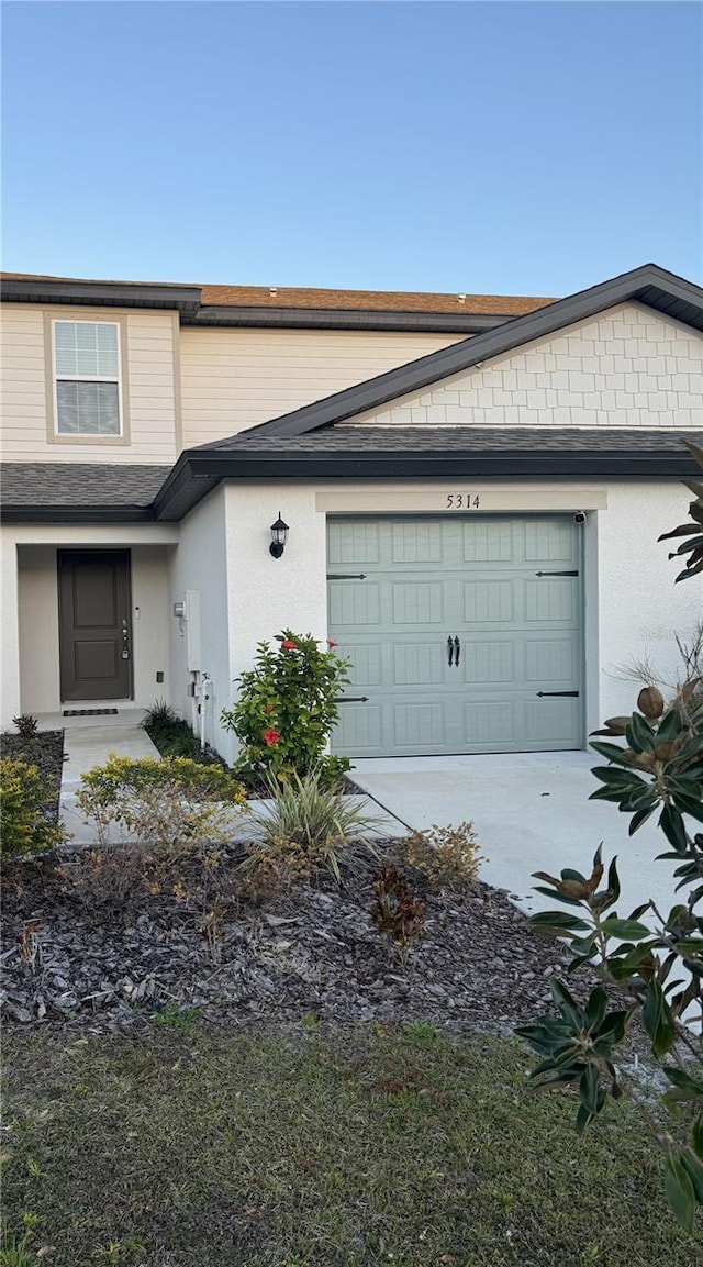 view of front of property featuring an attached garage, a shingled roof, and stucco siding