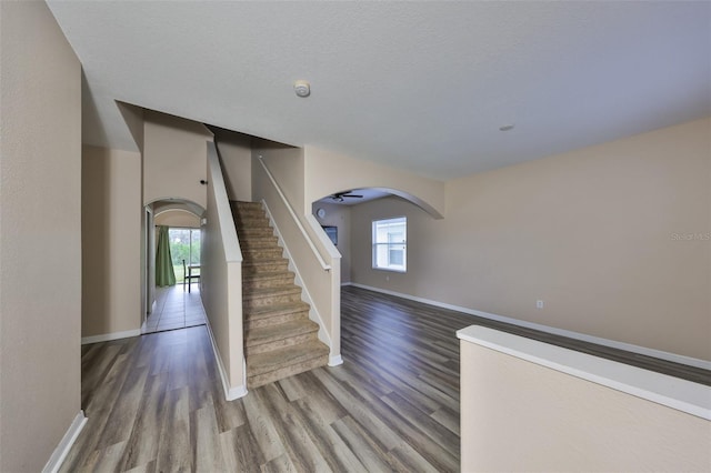 interior space with arched walkways, a textured ceiling, baseboards, and wood finished floors