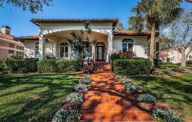 mediterranean / spanish-style home featuring a tiled roof, a front yard, a porch, and stucco siding