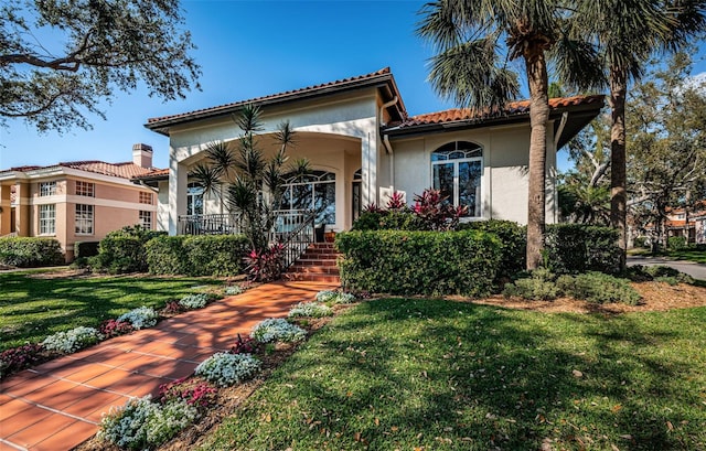 mediterranean / spanish-style house featuring covered porch, a tile roof, a front lawn, and stucco siding