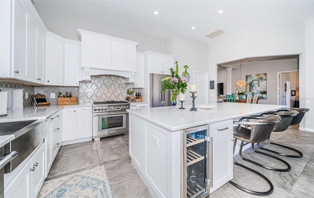 kitchen with a breakfast bar area, beverage cooler, white cabinetry, appliances with stainless steel finishes, and tasteful backsplash