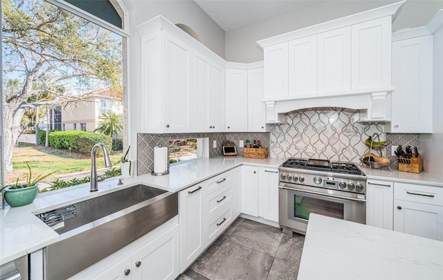 kitchen with white cabinets, decorative backsplash, a sink, and high end stainless steel range