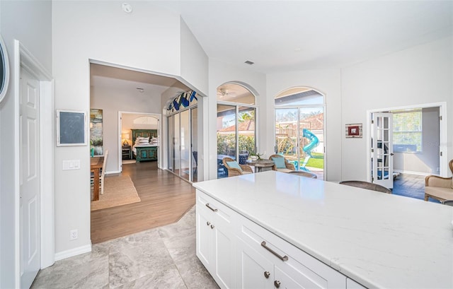 kitchen featuring baseboards, light stone counters, open floor plan, and white cabinets