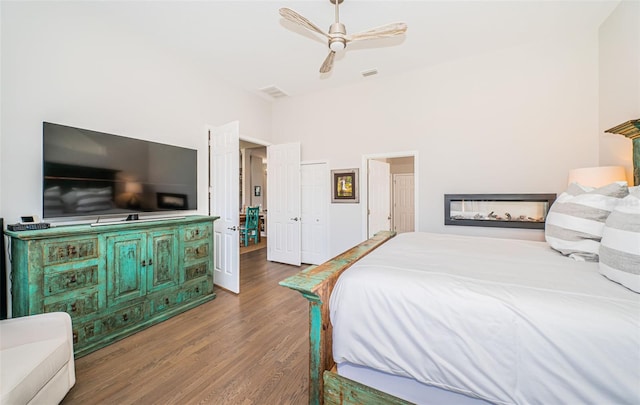 bedroom featuring ceiling fan, wood finished floors, visible vents, a multi sided fireplace, and a closet