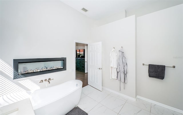 bathroom with marble finish floor, visible vents, a glass covered fireplace, a freestanding tub, and baseboards