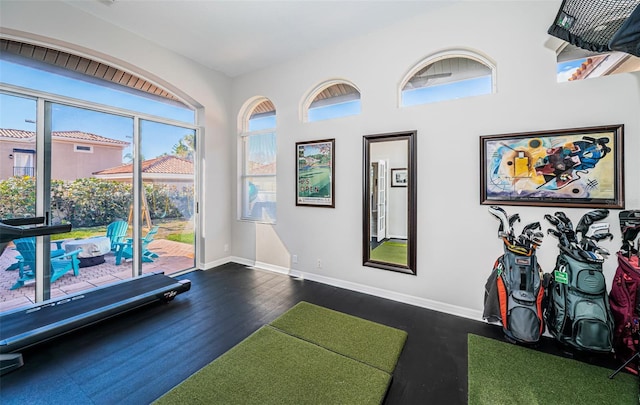 workout area featuring golf simulator, dark wood-style flooring, and baseboards