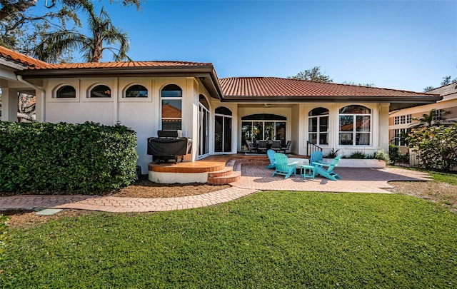 back of property featuring a patio area, a lawn, a tiled roof, and stucco siding