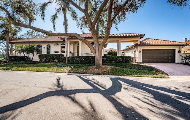 mediterranean / spanish house with decorative driveway, a tile roof, an attached garage, and stucco siding