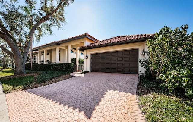 mediterranean / spanish-style home with an attached garage, a tile roof, decorative driveway, and stucco siding