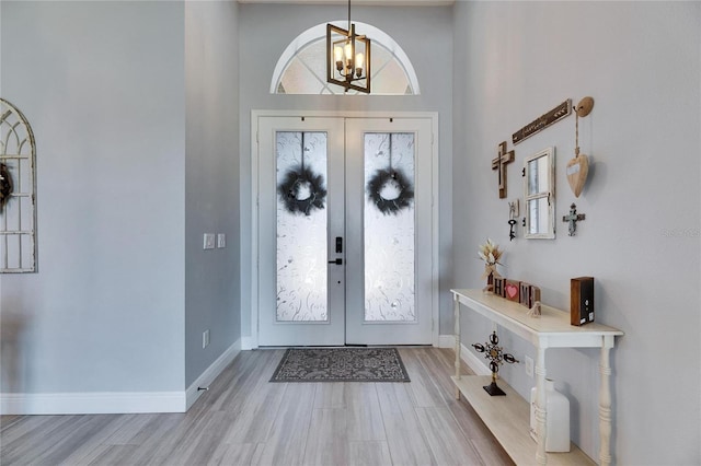 foyer featuring light wood finished floors, a notable chandelier, french doors, and baseboards