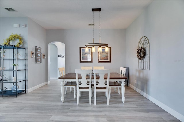 dining area featuring light wood-type flooring, arched walkways, visible vents, and baseboards