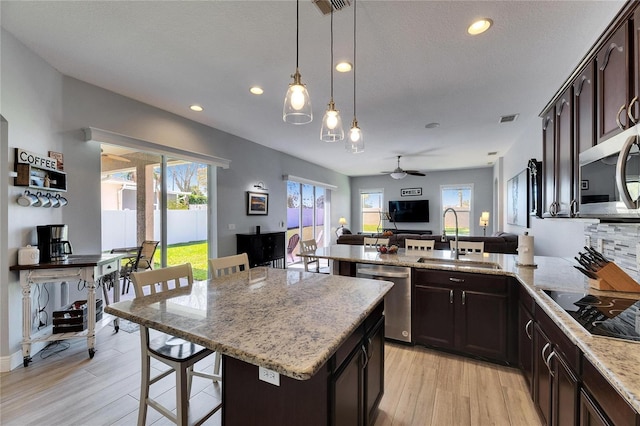 kitchen with open floor plan, light stone counters, a peninsula, stainless steel appliances, and a sink