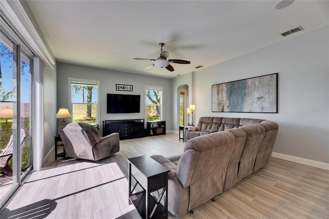 living room with visible vents, arched walkways, light wood finished floors, baseboards, and ceiling fan