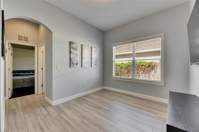 spare room with arched walkways, light wood-style floors, visible vents, and baseboards