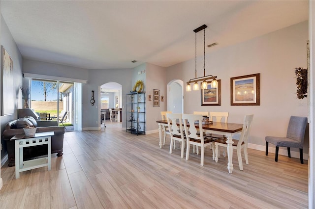 dining space with visible vents, light wood-style floors, arched walkways, and baseboards