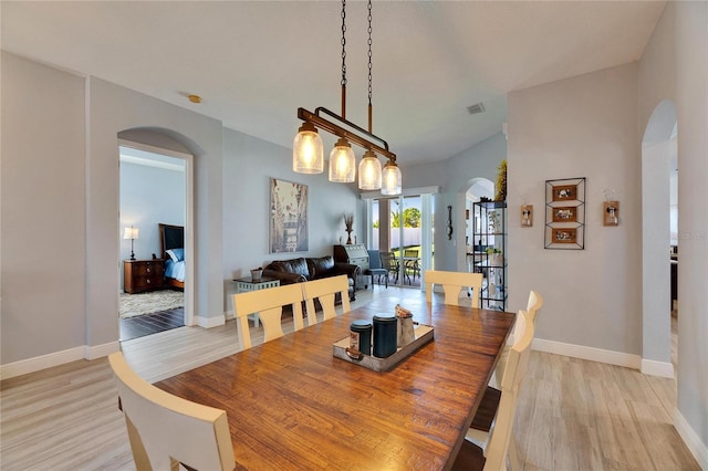 dining room featuring baseboards, light wood-type flooring, arched walkways, and visible vents