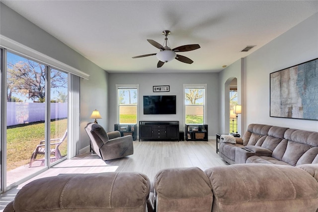 living area with visible vents, baseboards, light wood-type flooring, arched walkways, and a ceiling fan