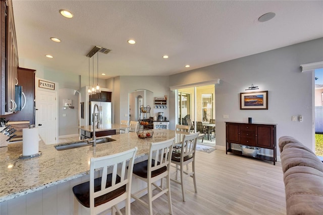 kitchen with a peninsula, arched walkways, stainless steel appliances, light wood-style floors, and a kitchen bar