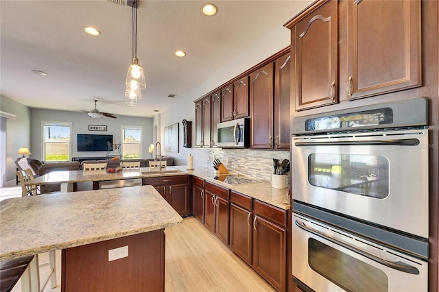 kitchen with decorative light fixtures, open floor plan, decorative backsplash, appliances with stainless steel finishes, and a sink