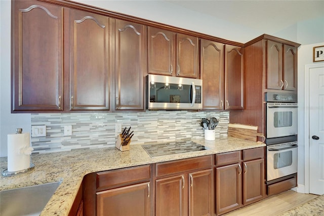 kitchen featuring light wood-style floors, stainless steel appliances, light stone countertops, and backsplash