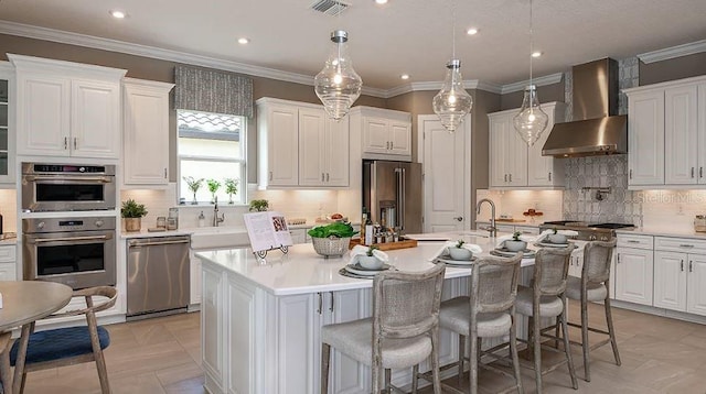 kitchen featuring stainless steel appliances, light countertops, white cabinets, an island with sink, and wall chimney exhaust hood