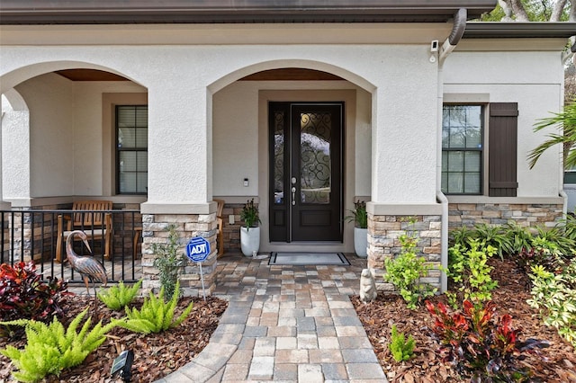 doorway to property featuring stone siding, covered porch, and stucco siding