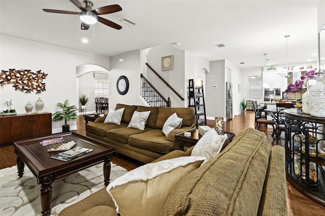 living room featuring dark wood-style floors, arched walkways, stairway, and ceiling fan with notable chandelier