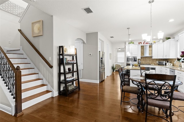 dining room with dark wood-style floors, arched walkways, visible vents, and stairway