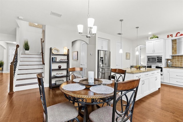 dining area with stairs, arched walkways, and wood finished floors