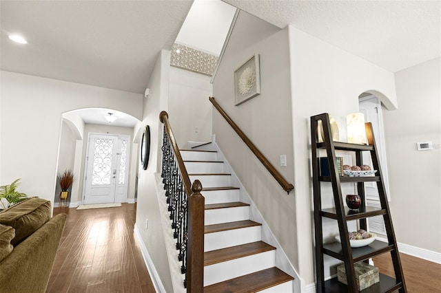 stairway with arched walkways, wood finished floors, and baseboards