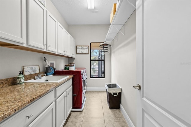 clothes washing area with light tile patterned floors, cabinet space, a sink, a textured ceiling, and washer and dryer