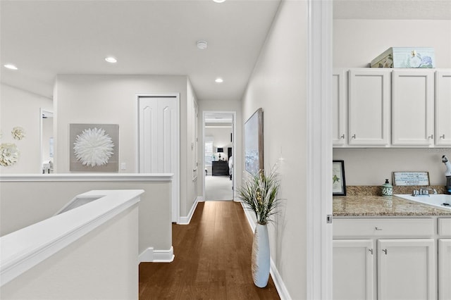 corridor featuring a sink, baseboards, dark wood-type flooring, and recessed lighting