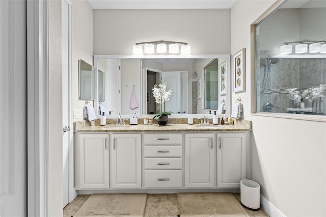 bathroom with double vanity, baseboards, walk in shower, and a sink