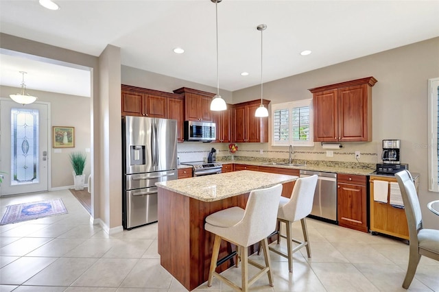 kitchen featuring stainless steel appliances, light stone countertops, a sink, and a kitchen island